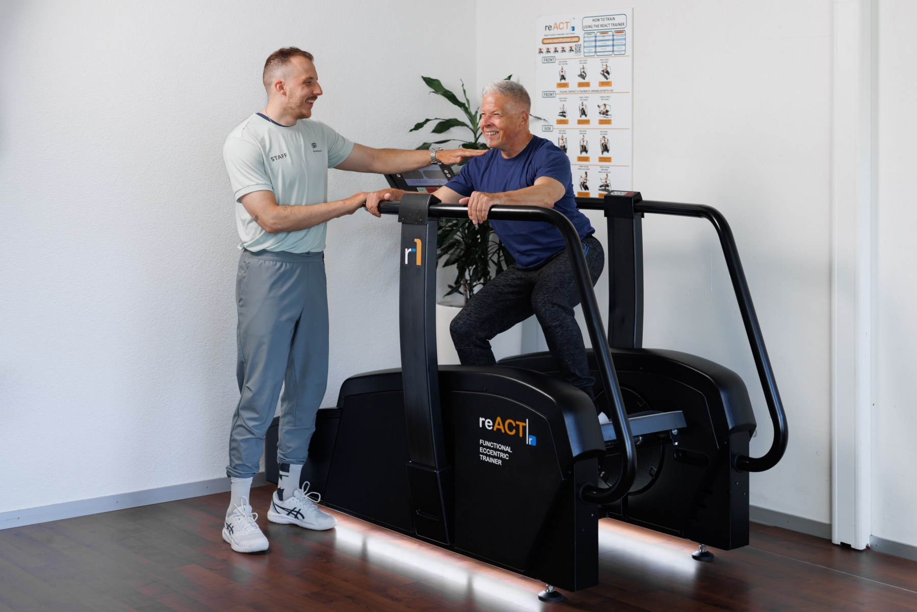 Ein Sportler trainiert auf dem reAct Trainer, während ein Trainer daneben steht und ihn anleitet.