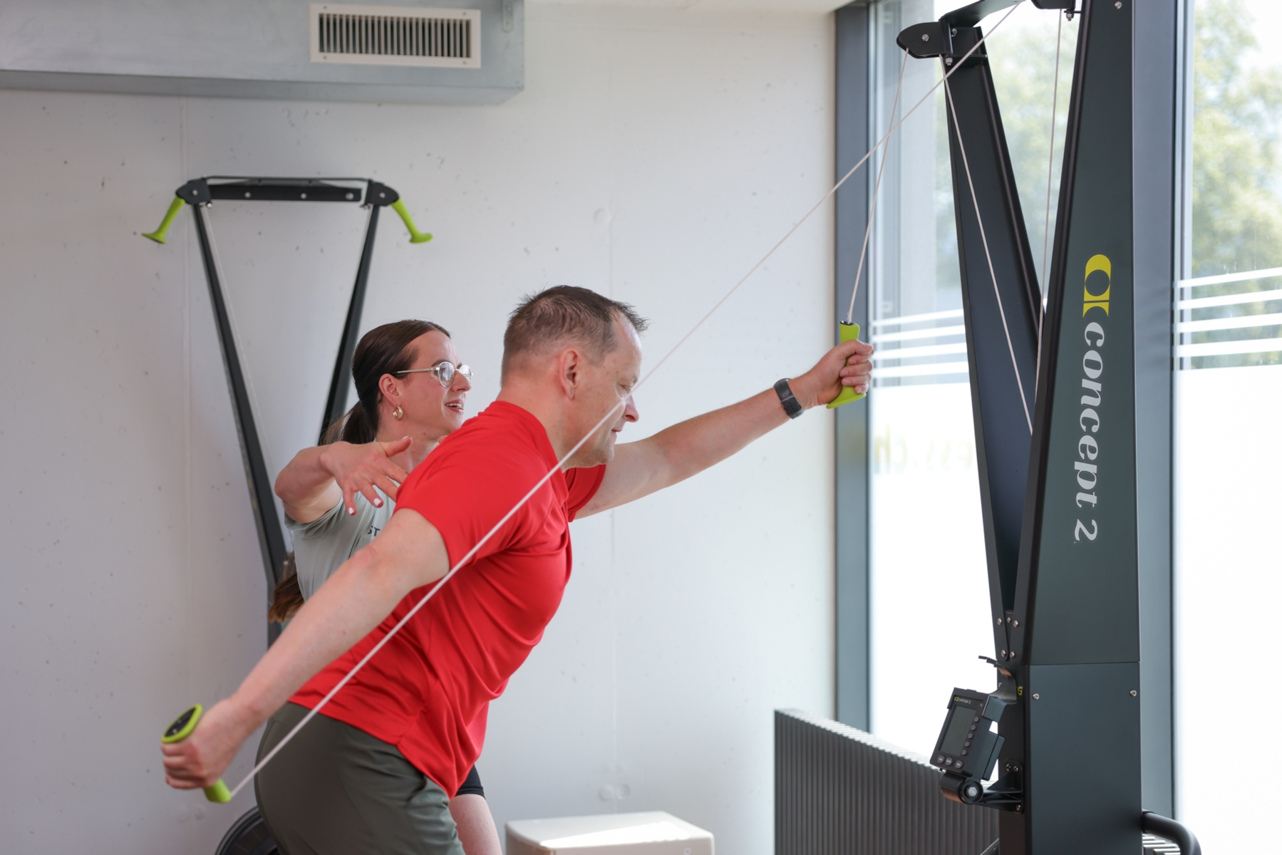 Eine trainierende Person nutzt ein Ski-Ergometer von Concept2, während eine Trainerin daneben steht und Anweisungen gibt.