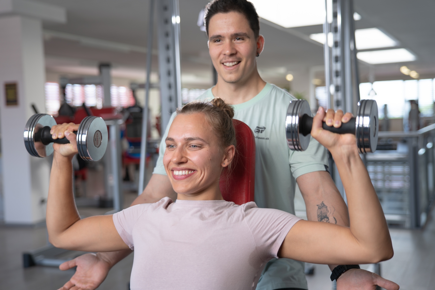 Trainer beim Instruieren einer Sportlerin beim Schulterdrücken mit Kurzhanteln